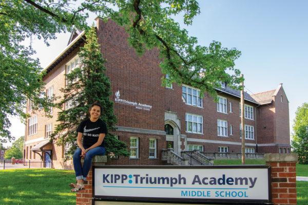 Carol Mendez '09 seated in front of St. Louis’ KIPP Triumph Academy.