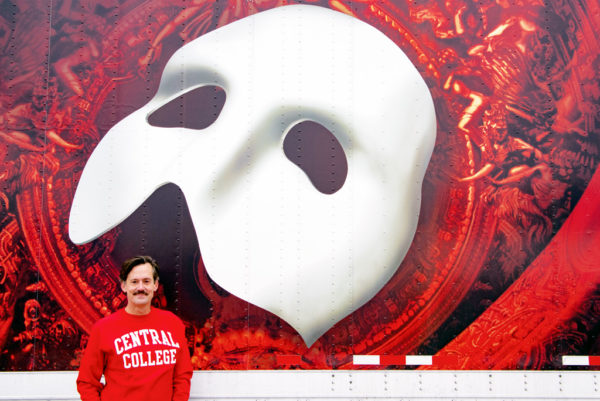 Rob Lindley '95 standing beside a trailer advertising "The Phantom of the Opera"